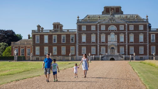 Family enjoying a summer day out at Wimpole, walking towards the camera with the hall behind them